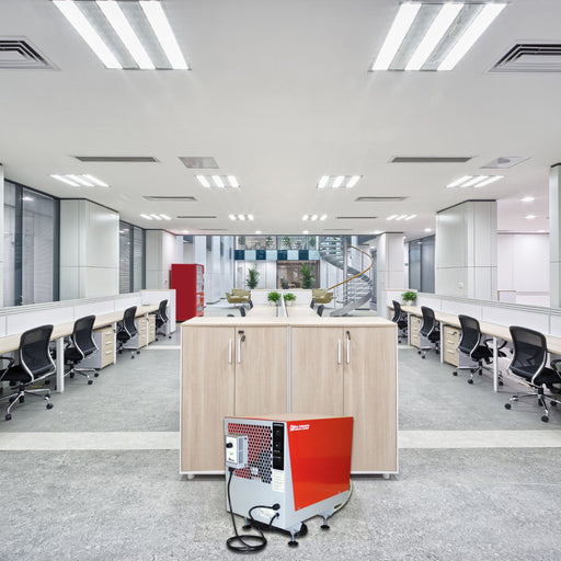 EBac CD60 commercial dehumidifier with a red and grey exterior is placed in a modern office environment, featuring multiple workstations and a staircase in the background.