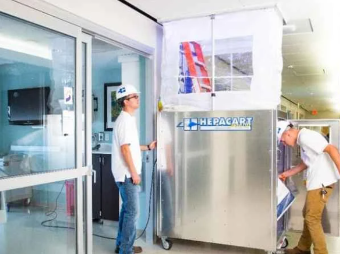 Two people installing the HEPACART  AutoLift Mobile Containment in a  hospital hall. 