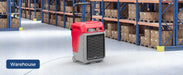 AlorAir Storm 80X commercial dehumidifier operating in a warehouse aisle between shelving units of stored boxes